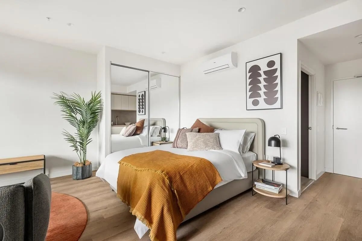 Bed with orange throw mirrored closet plant bedroom at Caulfield Place in Melbourne Student Accommodation