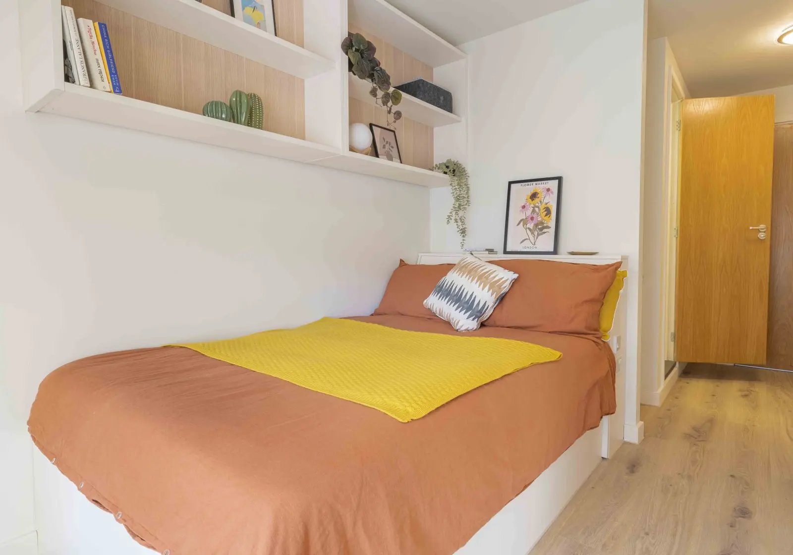 Bed with orange linens yellow throw pillows and shelves Bedroom at iQ Bristol in Bristol Student Accommodation