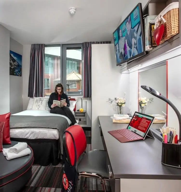 Woman reading on bed desk with laptop television bedroom at Study Inn Loughborough - Lemyngton Street in Loughborough Student Accommodation