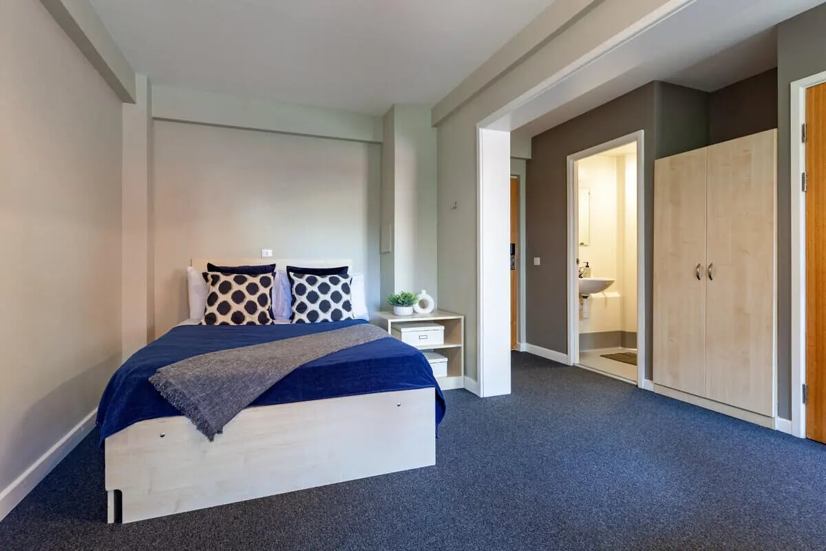 Bed with blue covers and patterned pillows bedroom closet and bathroom at The Forge in Sheffield Student Accommodation