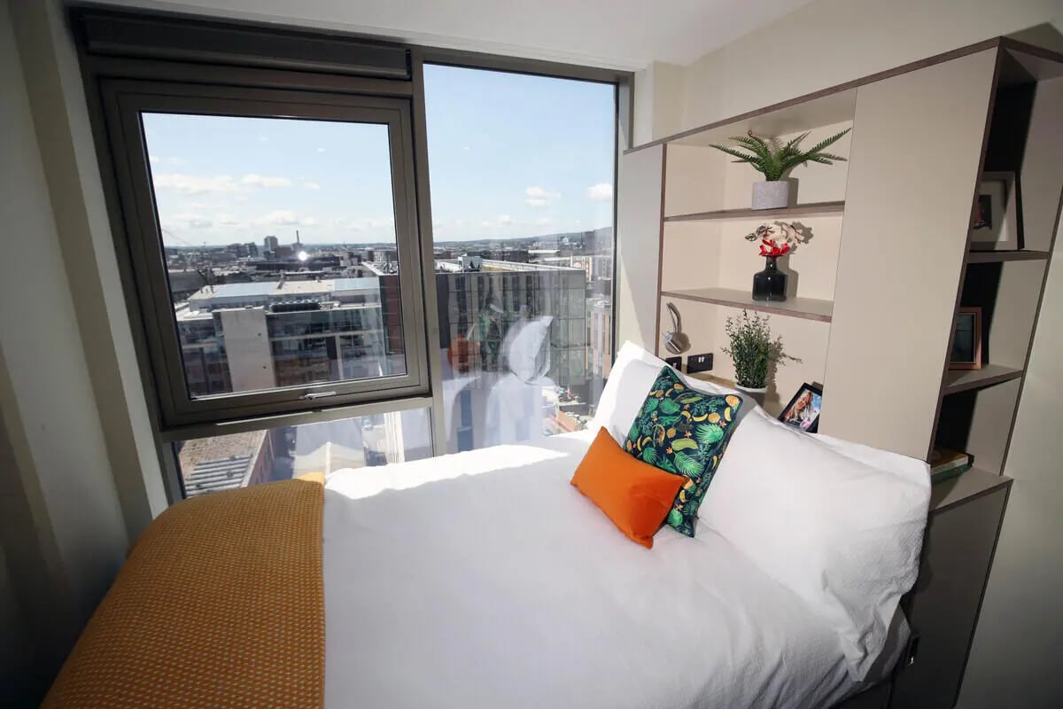 Bed pillows shelving with plants and city view bedroom at LIV Student Belfast in Belfast Student Accommodation