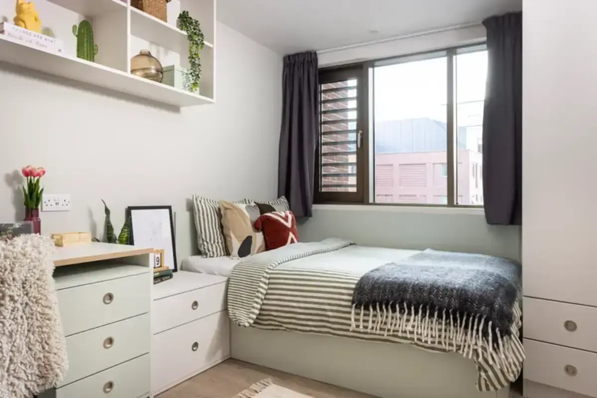 Bed with striped bedding desk and shelves bedroom at Hawthorne House in London Student Accommodation