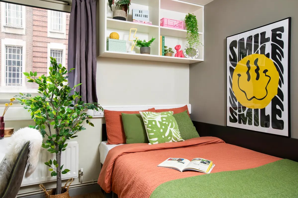 Bed with orange duvet green pillows smile poster bedroom at East Central House in London Student Accommodation