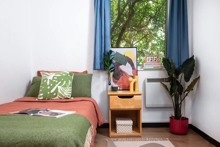 Bed with patterned pillows bedside table artwork radiator bedroom at Ewen Henderson Court in London Student Accommodation