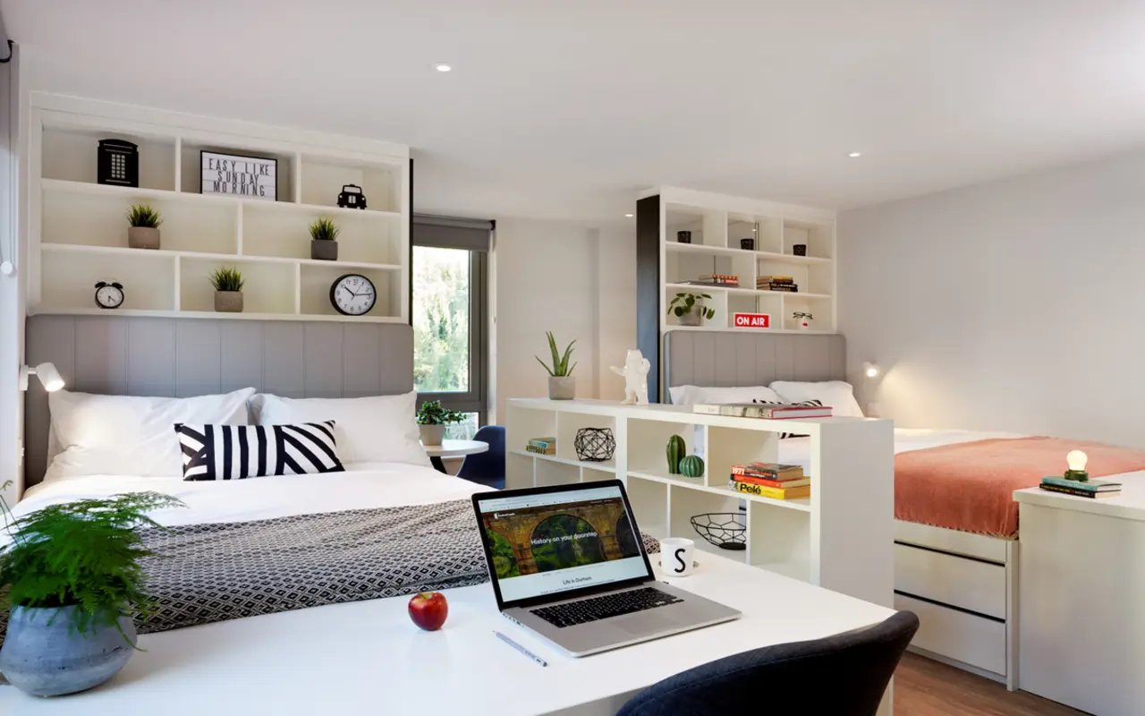 Two beds laptop desk plants shelves bedroom interior at Student Castle Durham in Durham Student Accommodation