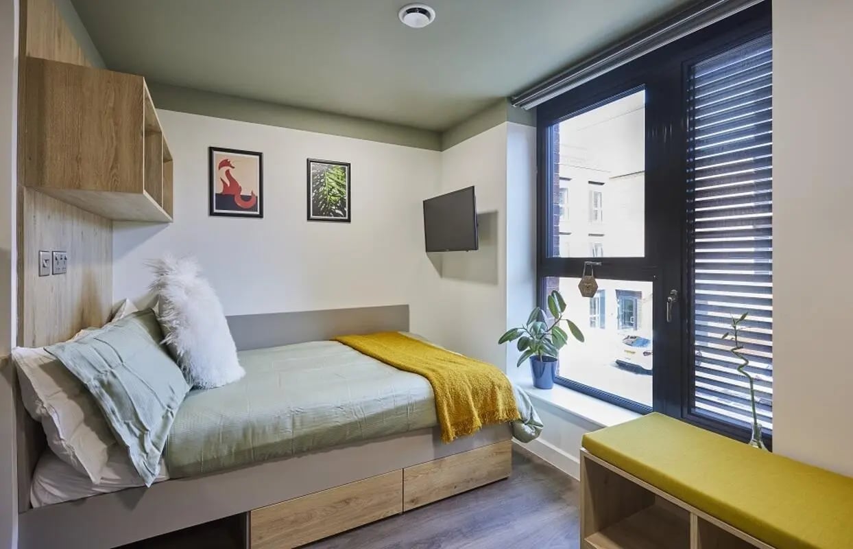 Bed with yellow throw bedside shelf tv bedroom at Regatta Place in Durham Student Accommodation