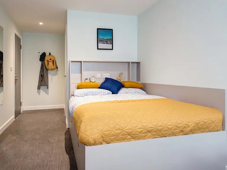 Bed with yellow blanket backpack on hook bedroom at Carrick View in Falmouth Student Accommodation