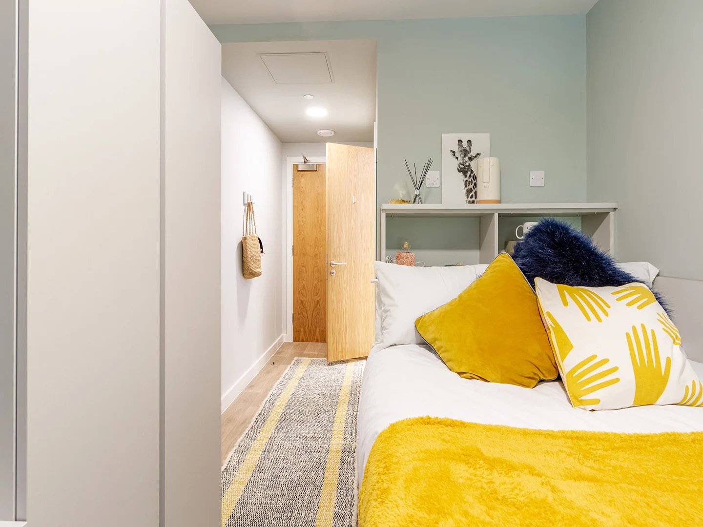 Bed with yellow pillows shelf and doors bedroom at The Refinery in Leeds Student Accommodation