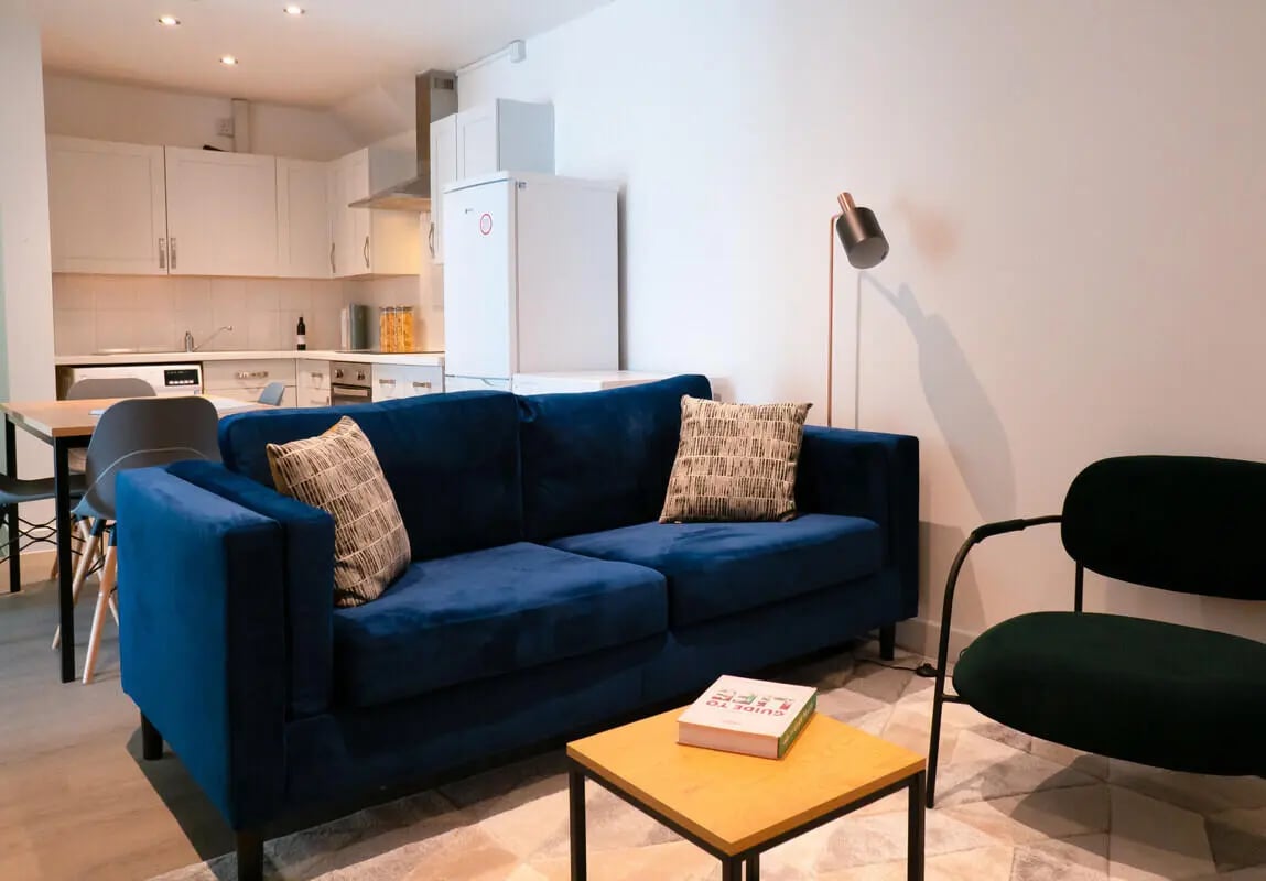 Blue sofa two pillows kitchen visible living room at 5 Bedroom House at Flat 1, 331, Dickenson Road in Manchester Student Accommodation