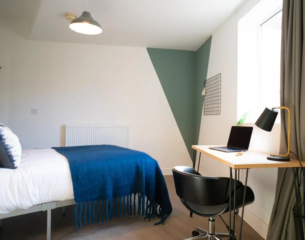 Bed with blue blanket laptop desk and chair bedroom at 5 Bedroom House at Flat 1, 331, Dickenson Road in Manchester Student Accommodation