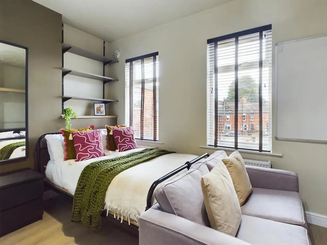 Bed with green throw pink pillows sofa bedroom at 7 Bedroom House at 19, Studios at, The Avenue in Lincoln Student Accommodation
