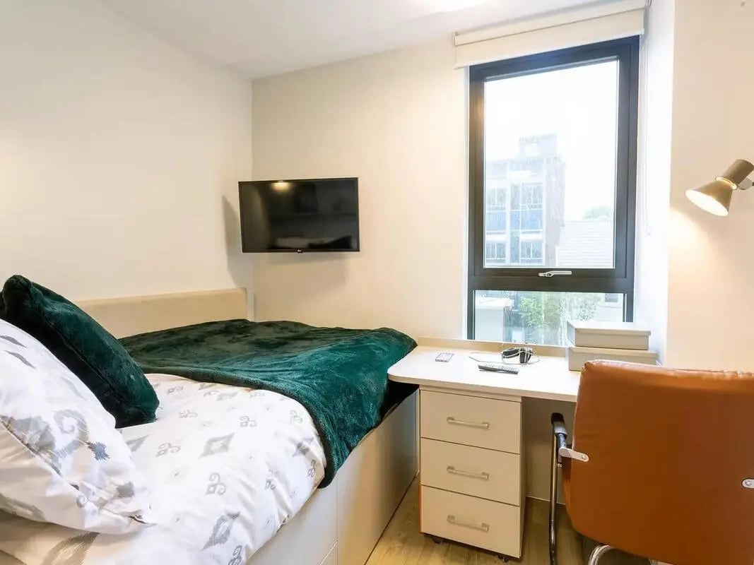 Bed with green throw TV desk with chair bedroom at SEREN in Swansea Student Accommodation