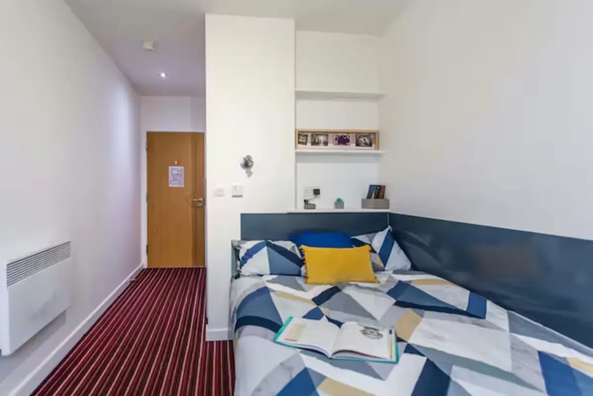 Bed with patterned duvet yellow pillow open book Bedroom at Brookland Road in Leicester Student Accommodation