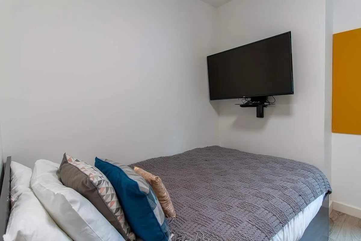 Bed with pillows mounted TV and yellow board bedroom at Goods Corner in Edinburgh Student Accommodation