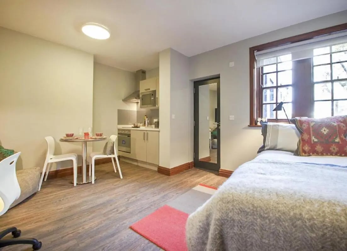 Bed kitchen dining area with white chairs studio apartment at Halsmere Studios in London Student Accommodation