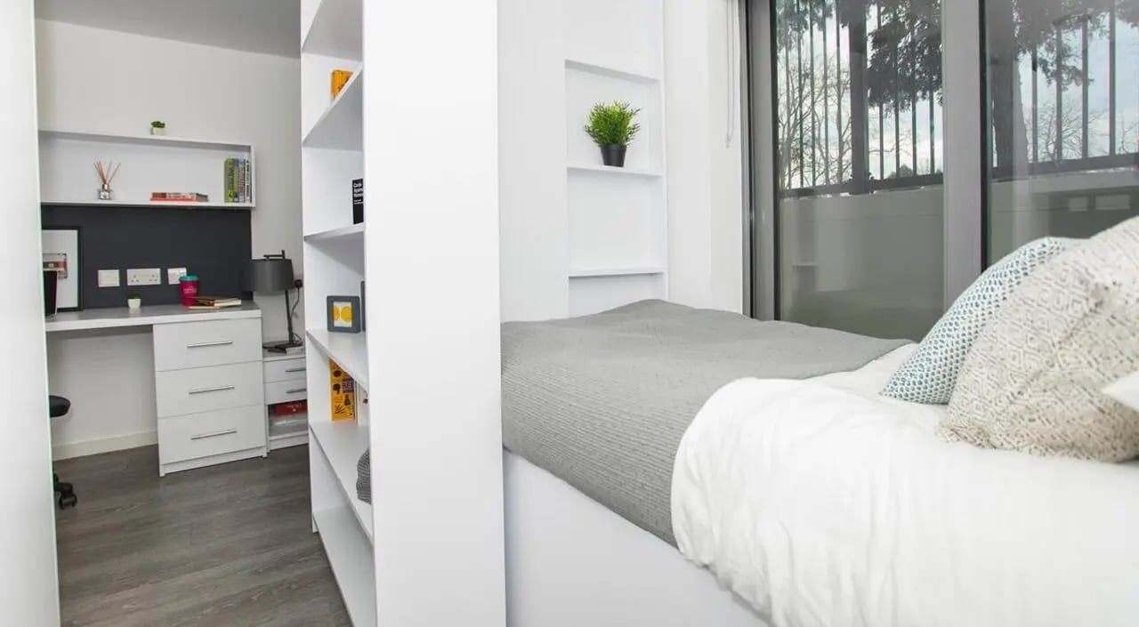 Desk bookshelves plant bed and pillows bedroom at The Cube Ealing in London Student Accommodation