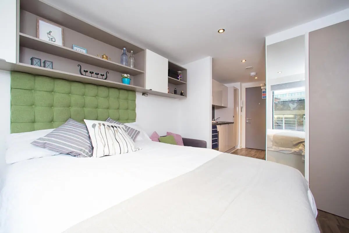 Bed with pillows shelves and kitchenette studio room at Primus Place in Leicester Student Accommodation