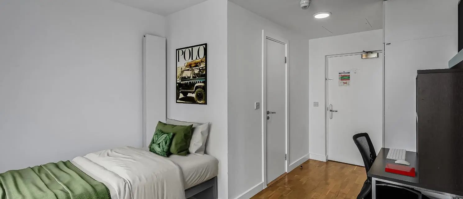 Bed with green pillows art desk with chair bedroom at Chapter Kings Cross in London Student Accommodation