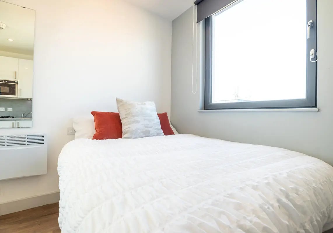 Bed with white comforter orange pillows bedroom at The Bridge Phase II in Newcastle Upon Tyne Student Accommodation