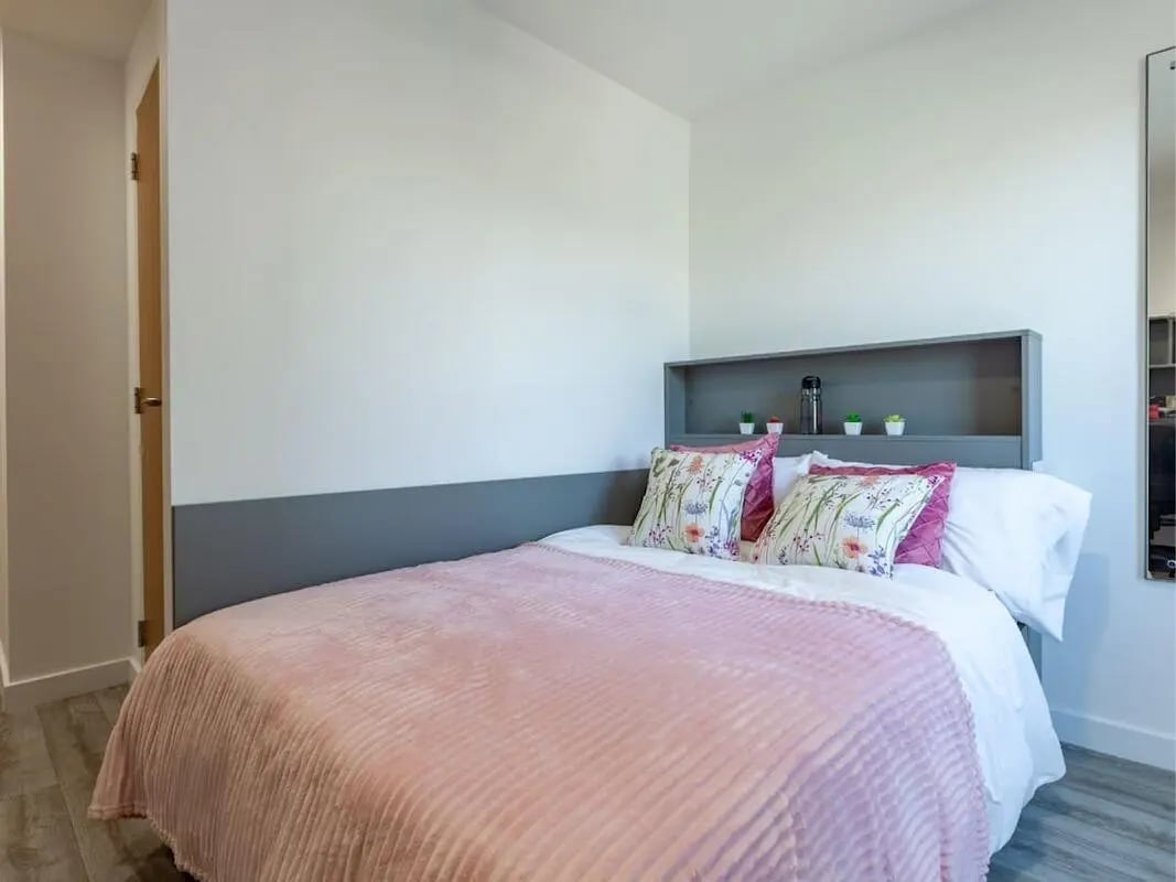 Bed with pink blanket patterned pillows shelf bedroom at The Oldway Centre in Swansea Student Accommodation