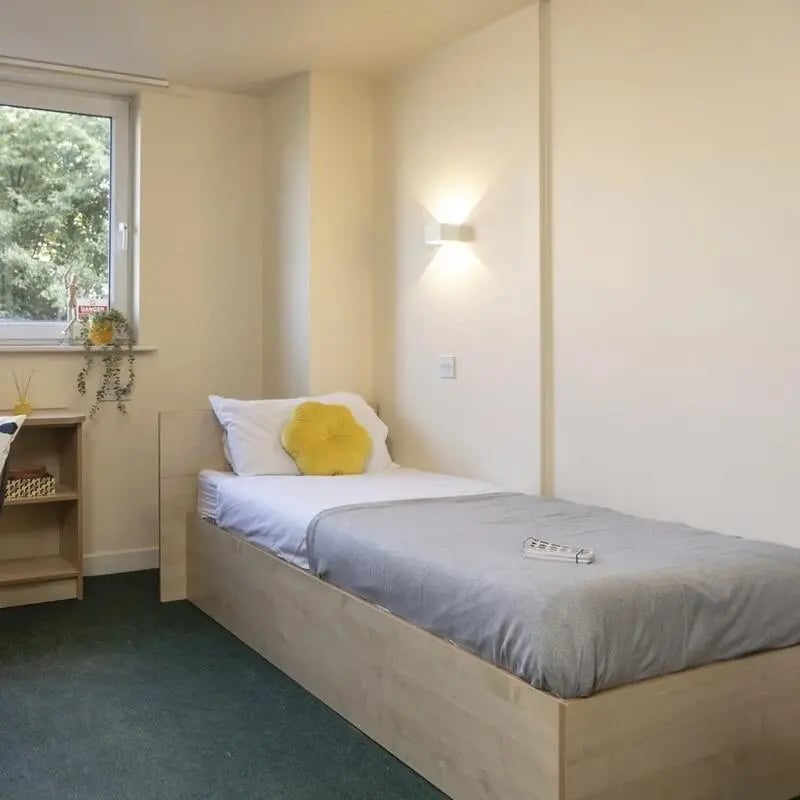 Bed with grey blanket yellow pillow bookcase bedroom at Burley Road in Leeds Student Accommodation