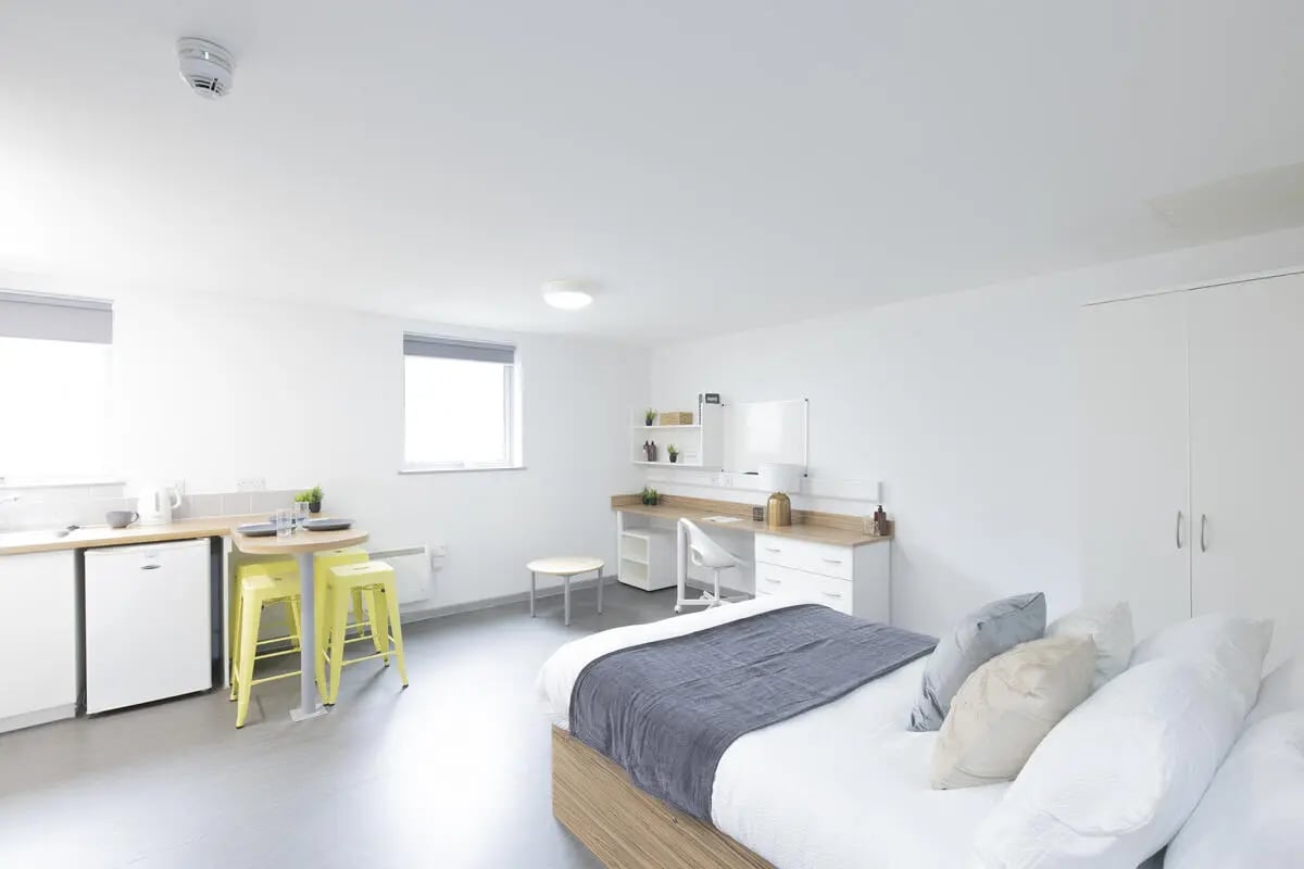 Bed desk kitchen area with yellow stools and bed. at Turner Court in Newcastle Upon Tyne Student Accommodation