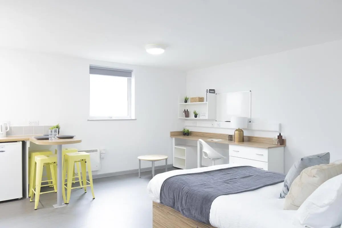 Bed desk kitchen area with yellow stools bedroom at Rosedale Court in Newcastle Upon Tyne Student Accommodation