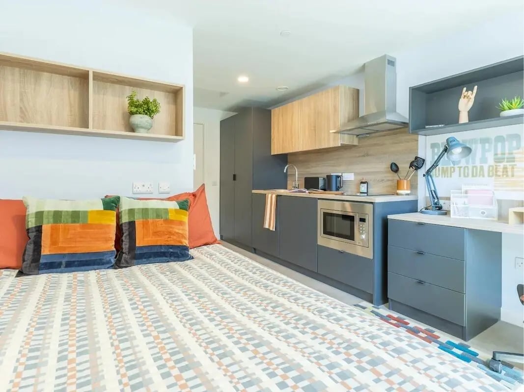Bed with colorful pillows kitchen and desk studio apartment at Croft Court in Bristol Student Accommodation