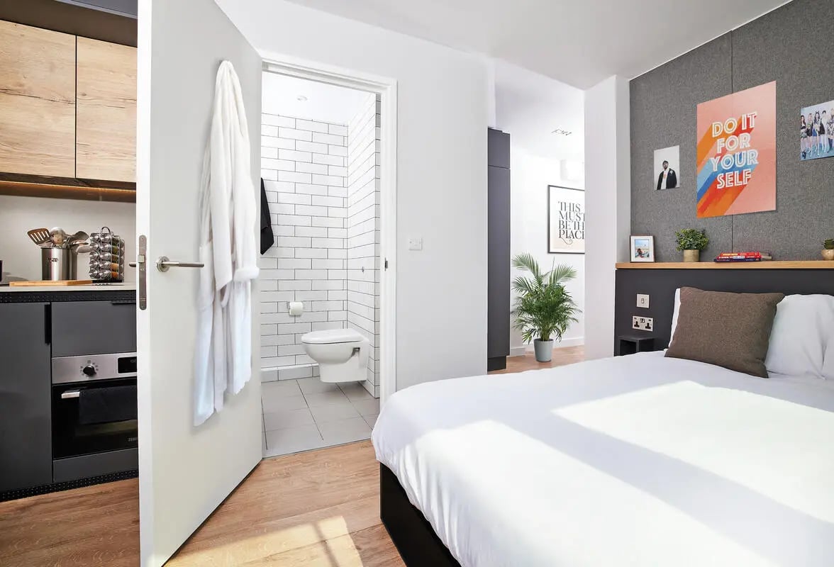 Bed white bathrobe open bathroom door kitchen bedroom at Vita Student Lewisham Exchange in London Student Accommodation