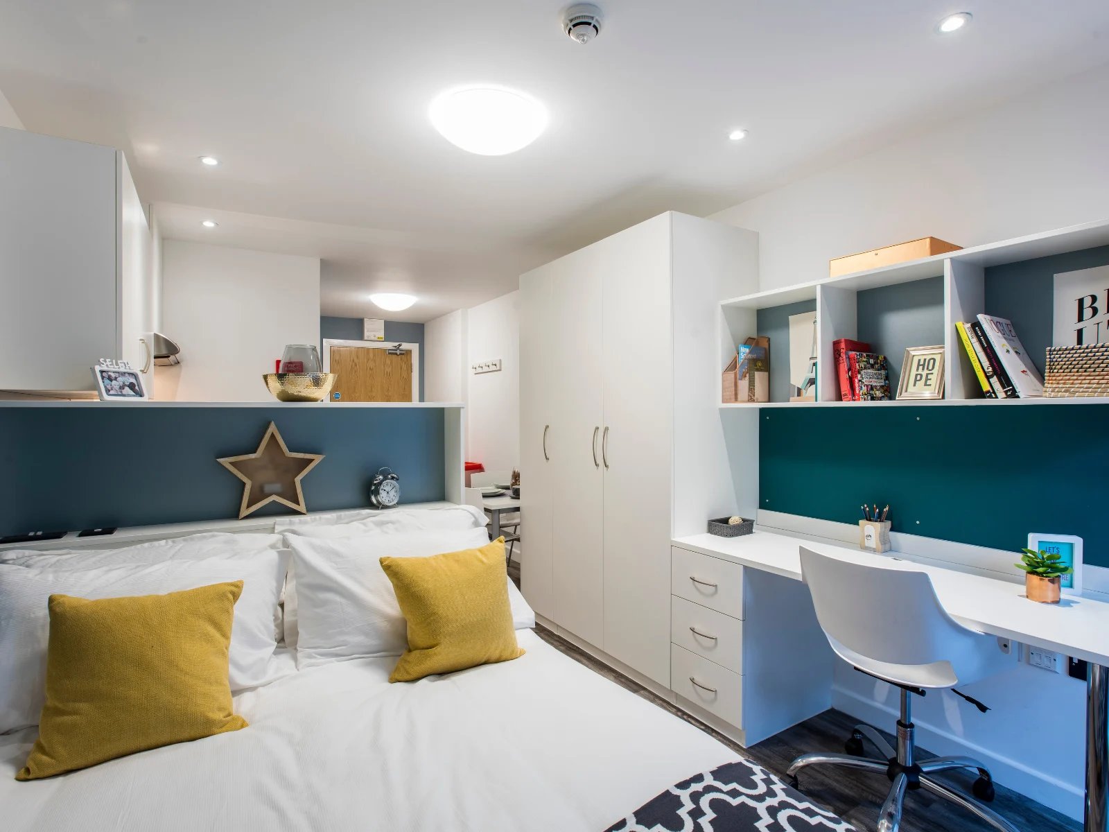 Bed with yellow pillows, desk, shelves, wardrobe bedroom at Botanic Studios in Belfast Student Accommodation