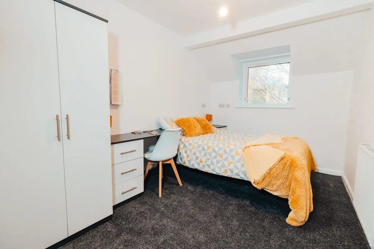 Wardrobe desk chair bed with orange pillows bedroom at Park Village in Sheffield Student Accommodation