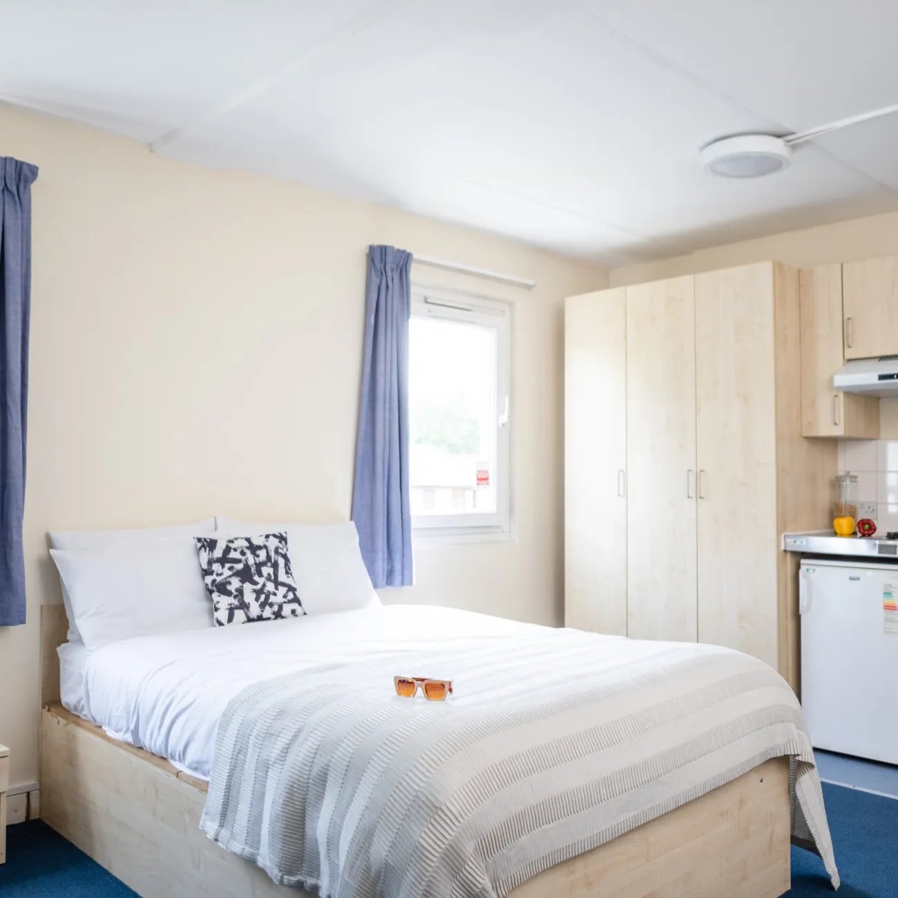 Bed with patterned pillow sunglasses and wardrobe kitchen area bedroom at Mcmillan student Village in London Student Accommodation