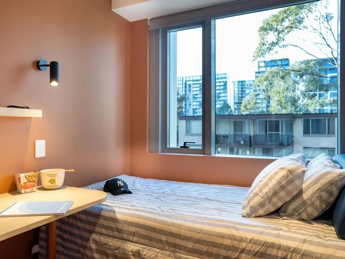Bed pillows desk with food and cap bedroom at The Switch Lachlan Macquarie Park in Sydney Student Accommodation