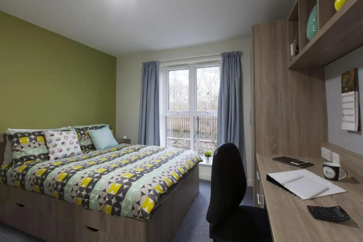 Bed with patterned bedding desk with chair and calculator bedroom at Selly Oak Court in Birmingham Student Accommodation