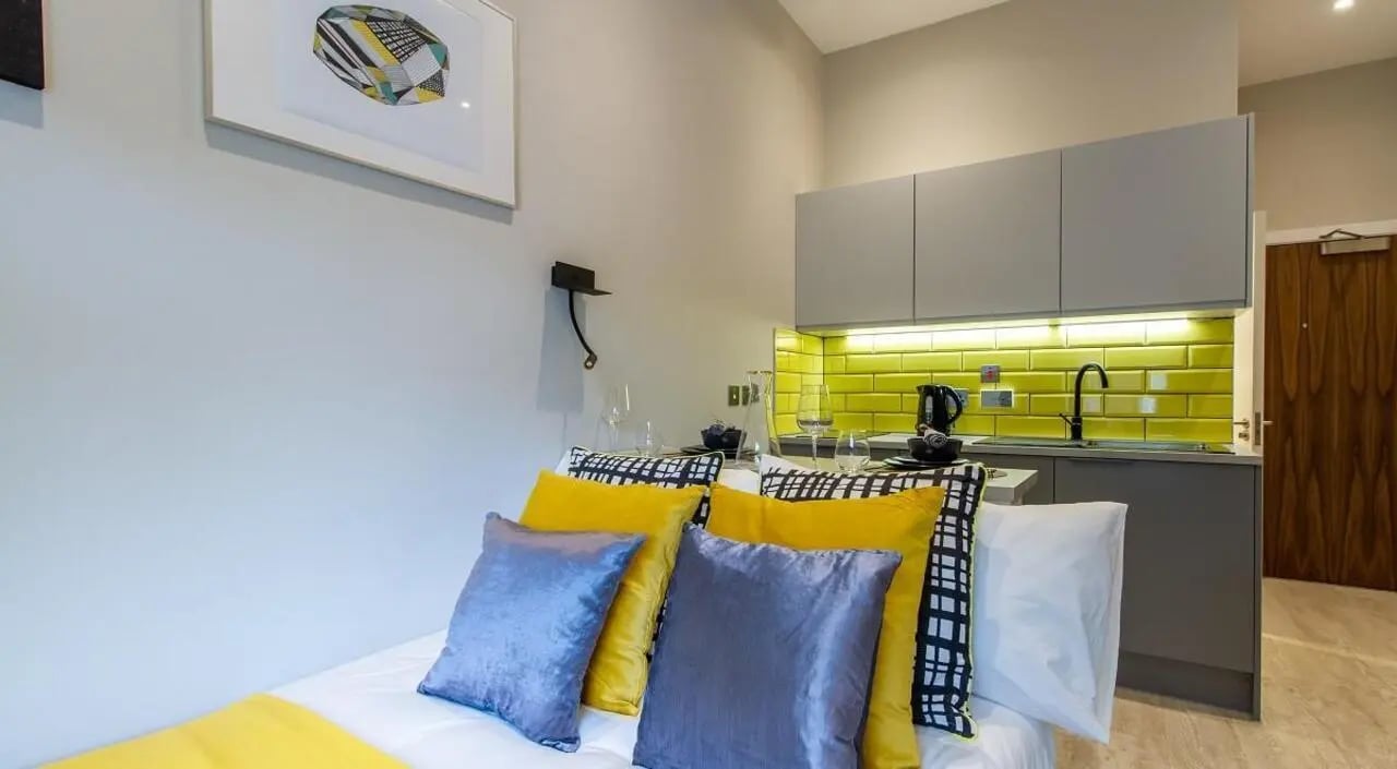 Bed with yellow and gray pillows kitchen area bedroom at AXO Seven Sisters in London Student Accommodation