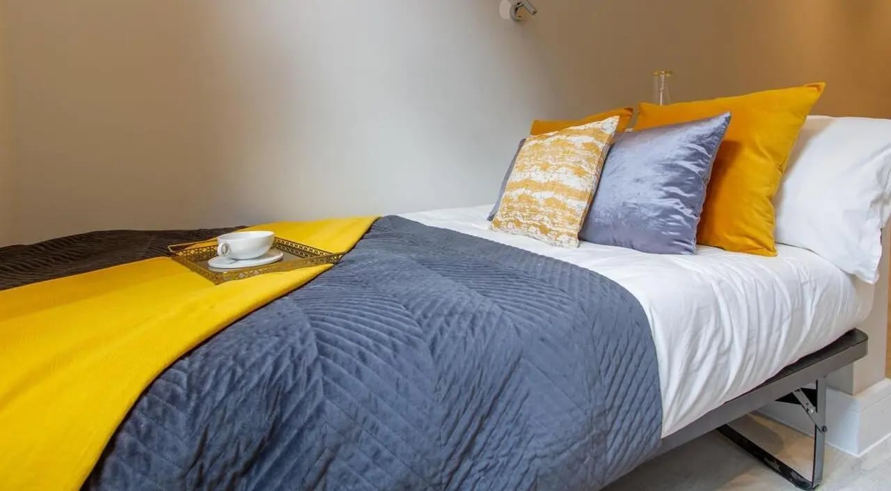 Bed with yellow blanket and pillows bedroom at AXO Seven Sisters in London Student Accommodation