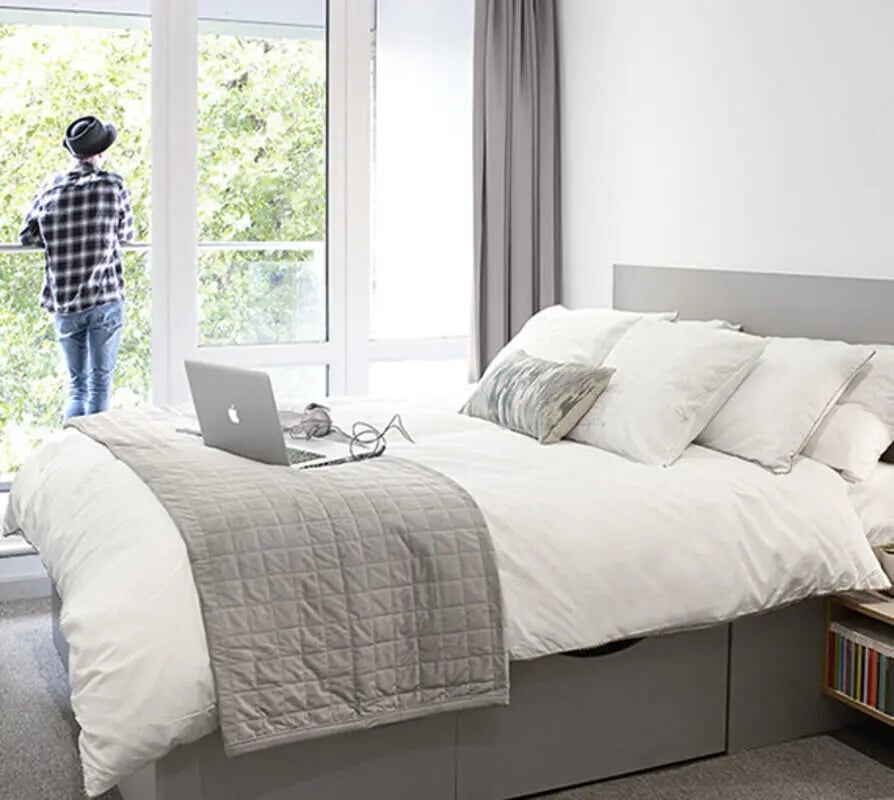 Bed with laptop and person at window bedroom at Lace Market Studios in Nottingham Student Accommodation