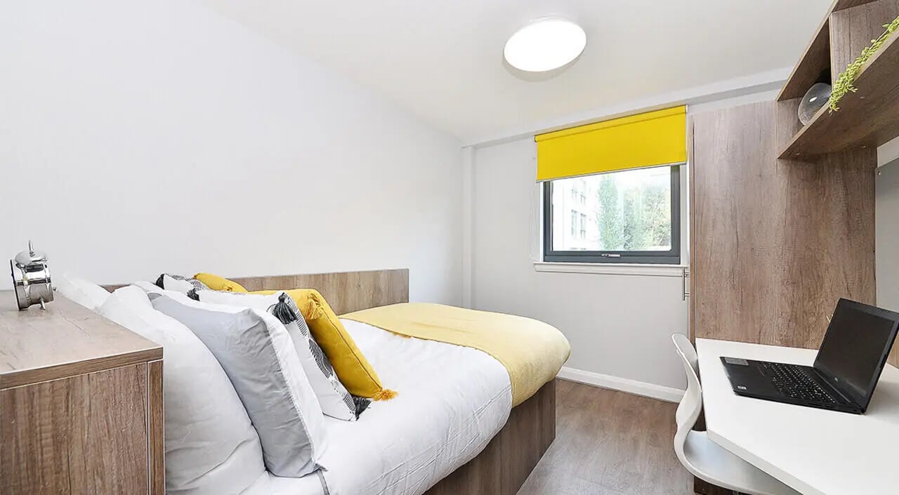 Bed with yellow throw and pillows desk laptop bedroom at The Mill House in Edinburgh Student Accommodation