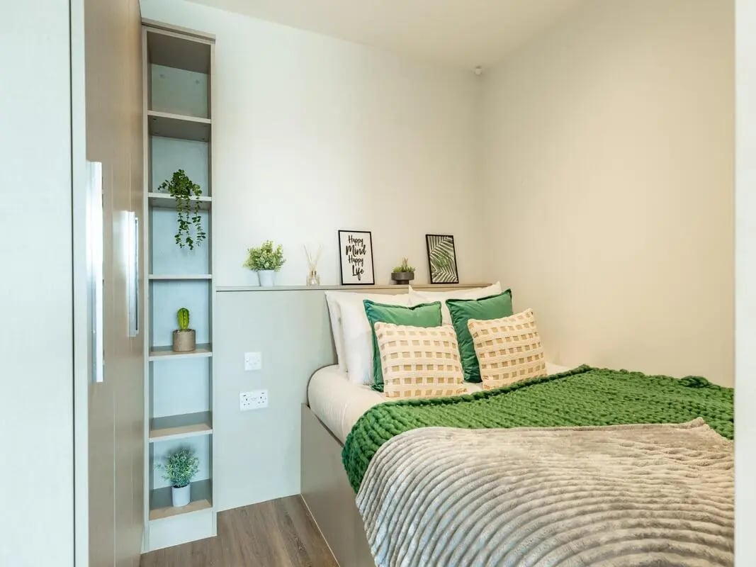 Bed with green blanket plants and shelves bedroom at Redvers Tower in Sheffield Student Accommodation