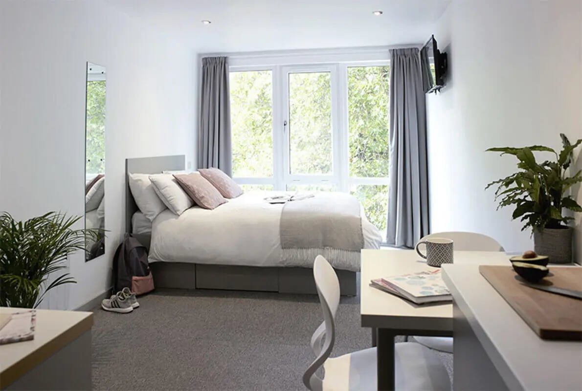 Bed with pillows and plants desk with mug bedroom at Lace Market Studios in Nottingham Student Accommodation