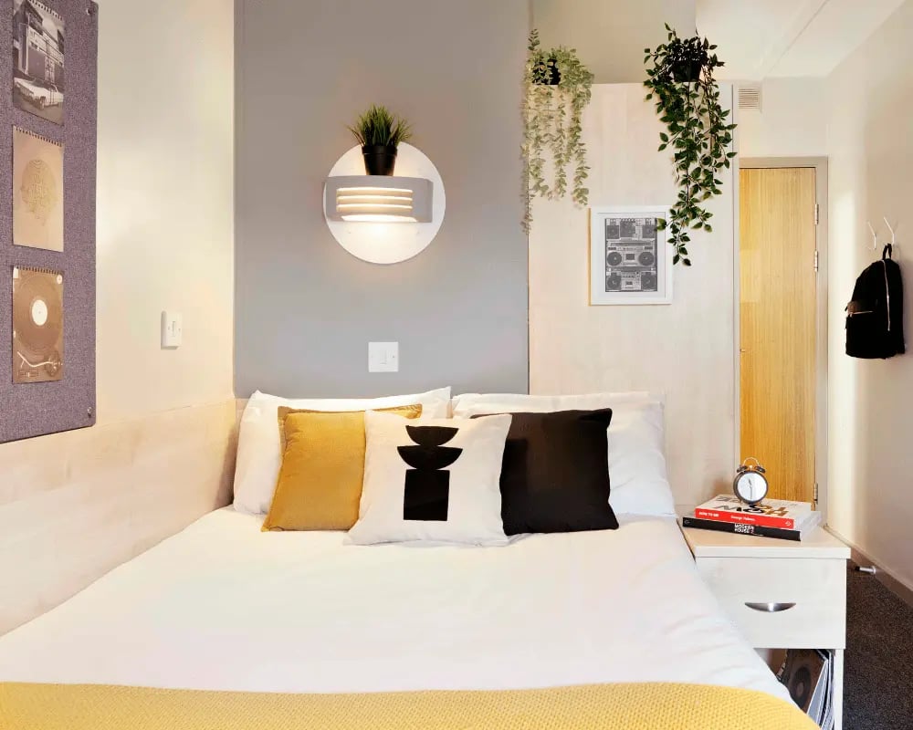 Bed pillows plants artwork backpack and bedside table bedroom at St Thomas Court in Plymouth Student Accommodation