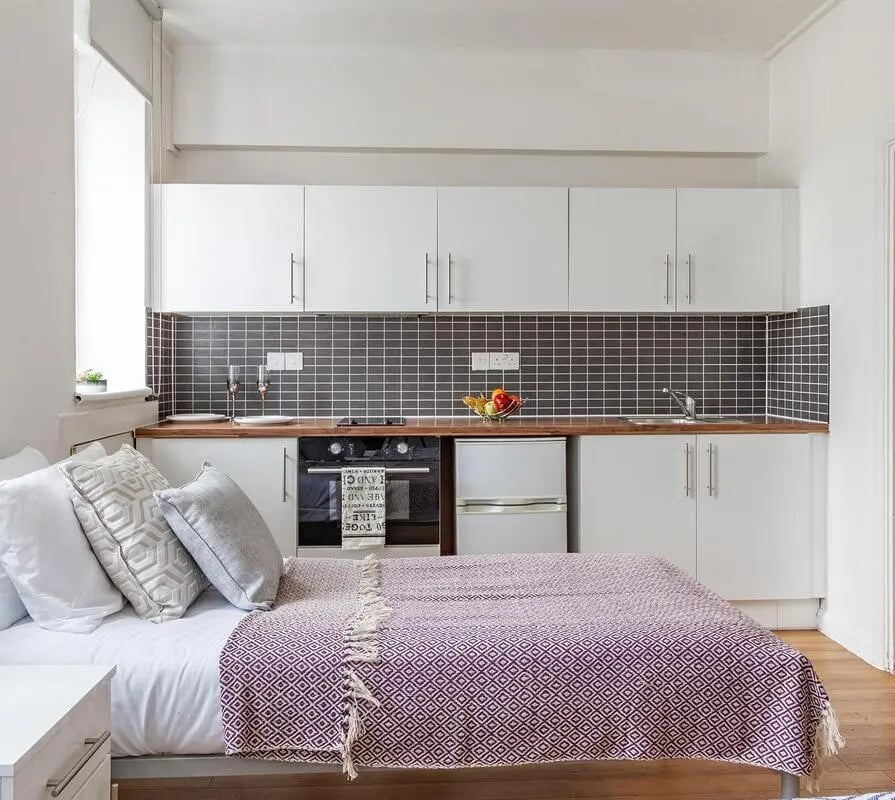 Bed with purple throw kitchen counter and cabinets studio apartment at Portobello Garrow House in London Student Accommodation