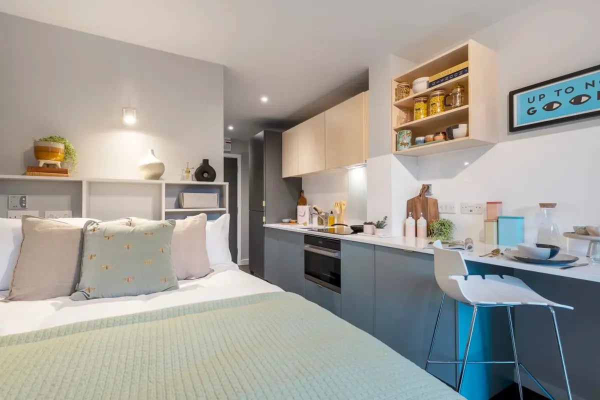 Bed with pillows kitchen counter and stool studio apartment at The Aspen in Leicester Student Accommodation
