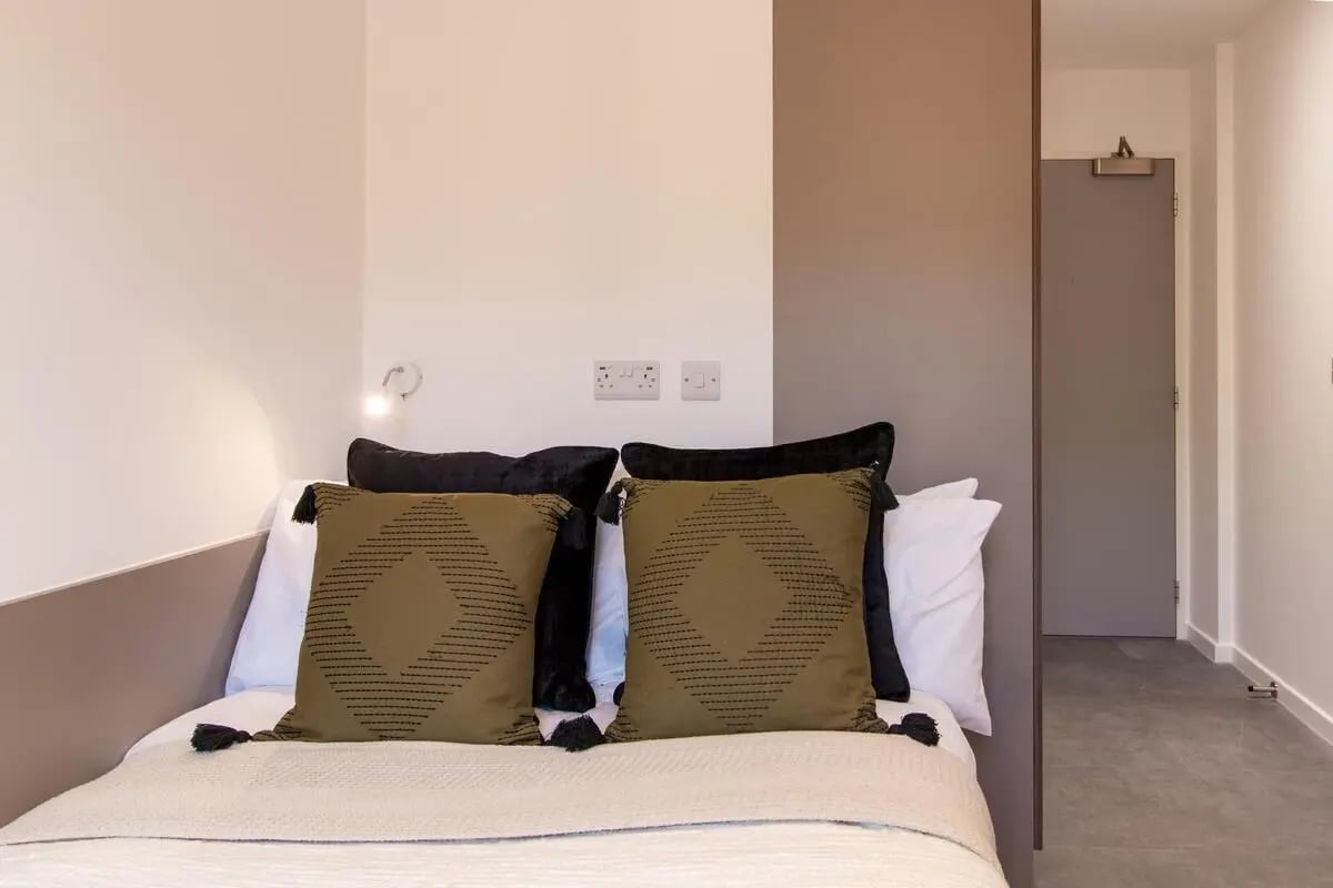 Bed with decorative pillows and hallway view Bedroom at Dean Street Works in Bristol Student Accommodation