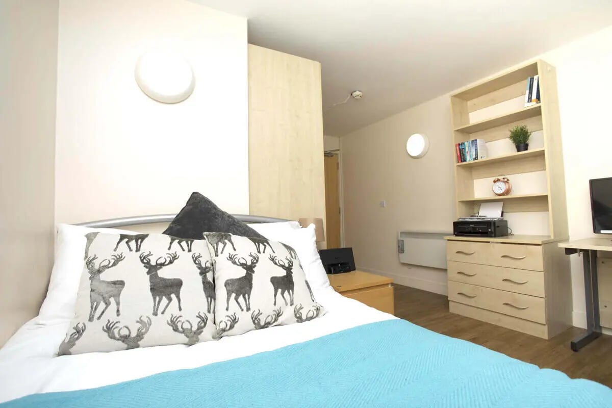Bed with deer pillows dresser printer bookshelf bedroom at Daisybank Villas in Manchester Student Accommodation