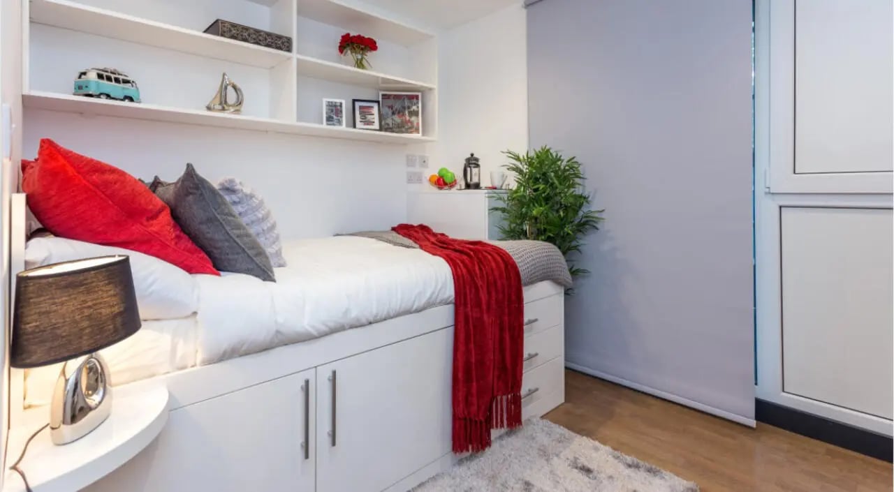 Bed with red and grey pillows and shelves Bedroom at The Court Yard in Southampton Student Accommodation