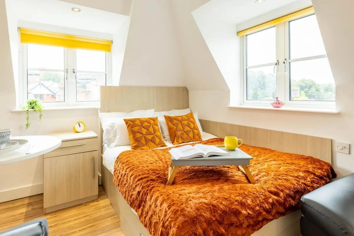 Bed with orange throw yellow pillows book tray study area at Iron Bridge Studios in Exeter Student Accommodation