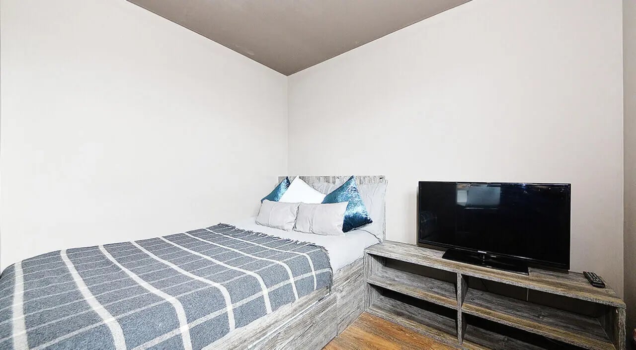 Bed with grey blanket TV on rustic stand bedroom at Marketgait Apartments in Dundee Student Accommodation