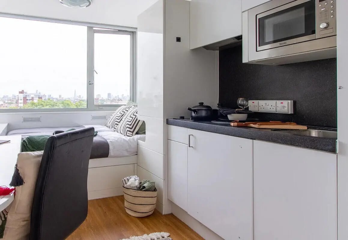 Bed with patterned pillows and kitchen counter Kitchen at Chelsea Lightfoot Hall in London Student Accommodation