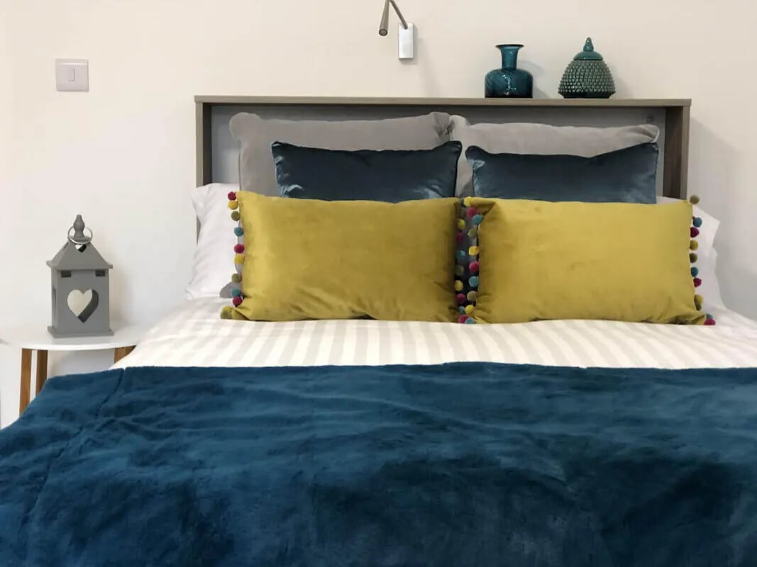 Bed with yellow teal pillows and blue throw bedroom at Q Studios in Stoke-On-Trent Student Accommodation